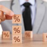 Homem de terno empilhando blocos com símbolo de porcentagem, representando a variação da taxa Selic e o funcionamento do Tesouro Selic